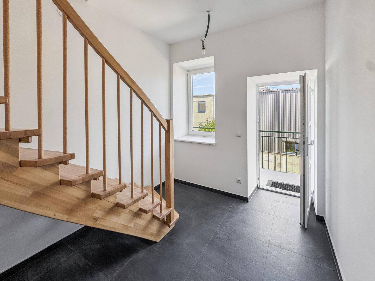 Eingangsbereich mit Holztreppe, Fliesenboden und Fenster, führt direkt ins Freie.