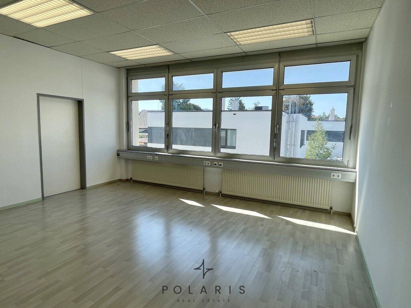 Geräumiger Bürobereich mit hellem Laminatboden und einer Fensterfront, die den Raum mit natürlichem Licht durchflutet.