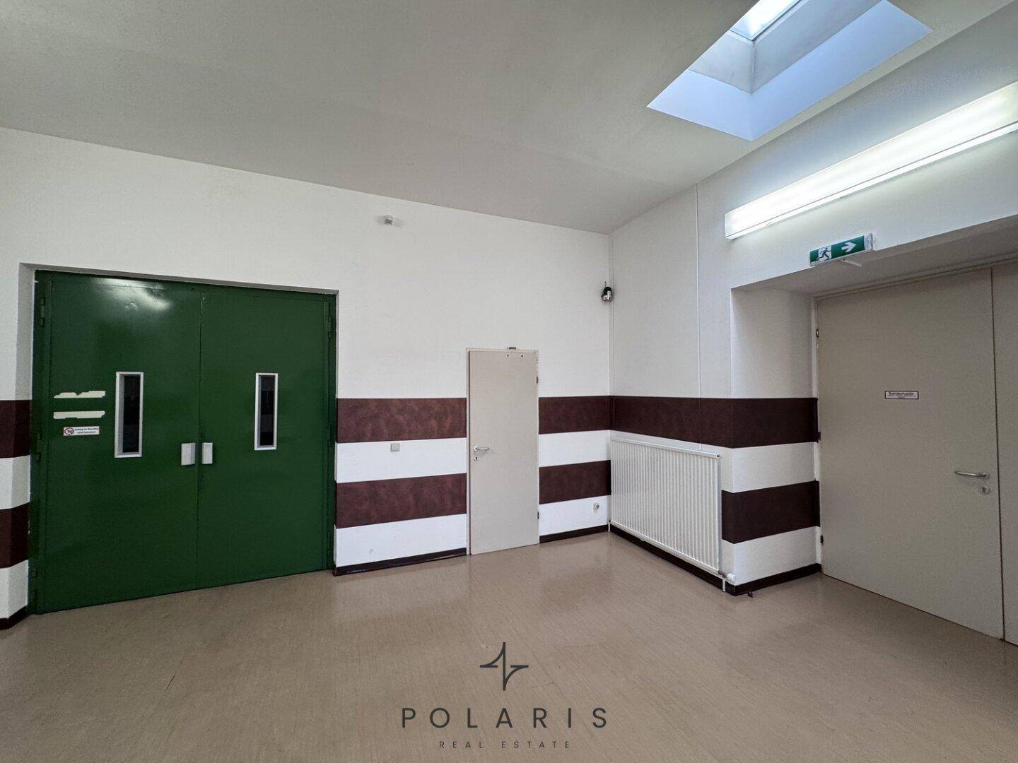 Treppenabsatz mit großer grüner Doppeltür, weiteren Türen, einem Heizkörper und einer Überwachungskamera.