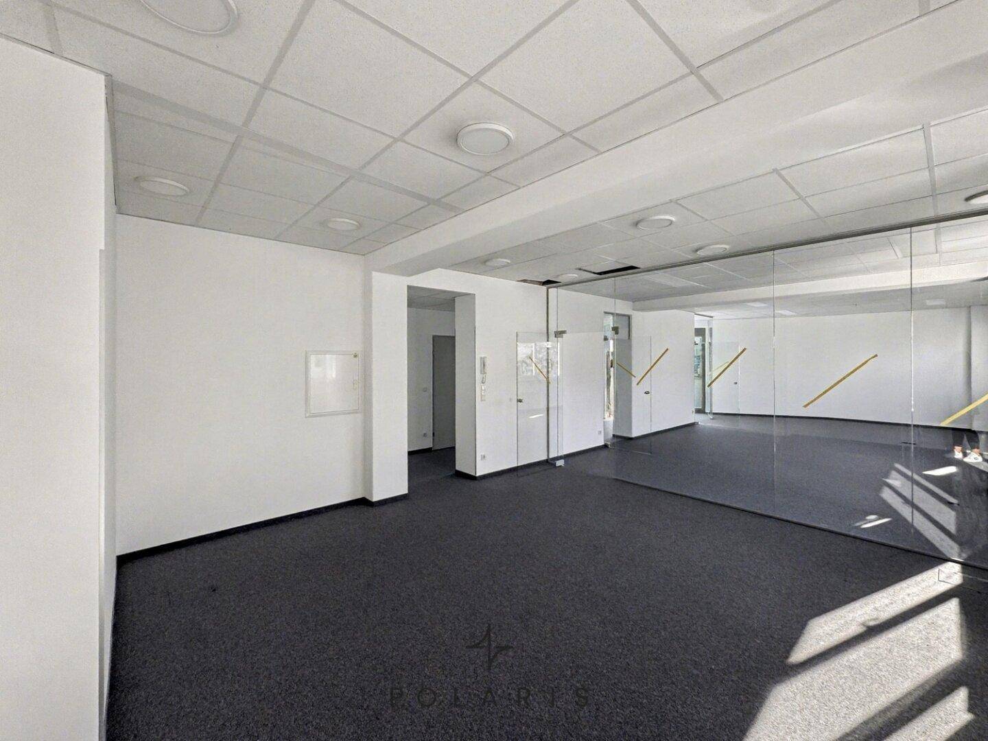 Großzügiger, leerer Büroraum mit Teppichboden und Glaswänden, ideal für flexible Arbeitsplatzgestaltung.