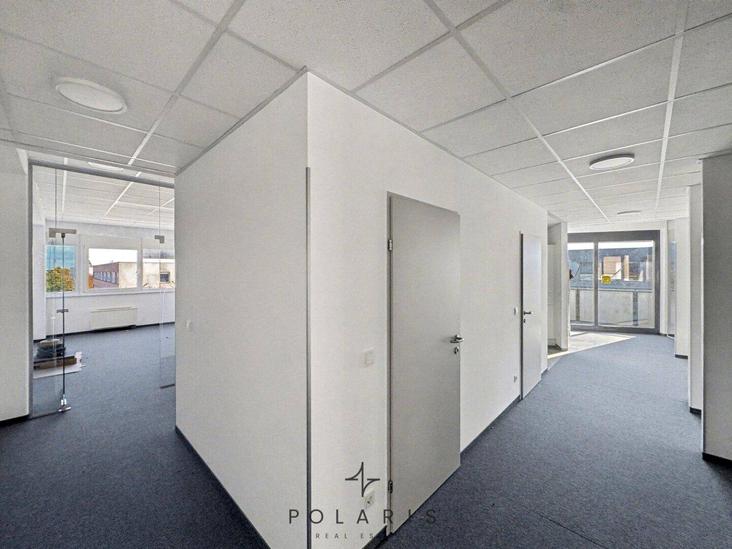 Heller Bürogang mit Teppichboden und Türen, der zu verschiedenen Büroräumen führt.