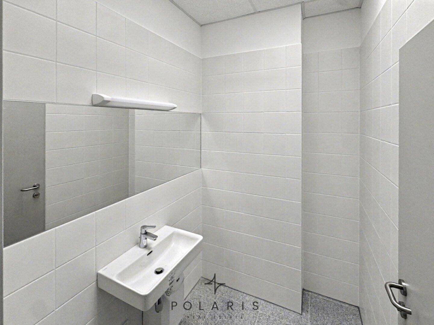 Helles Badezimmer mit weißen Wandfliesen, modernem Waschbecken und großem Spiegel.