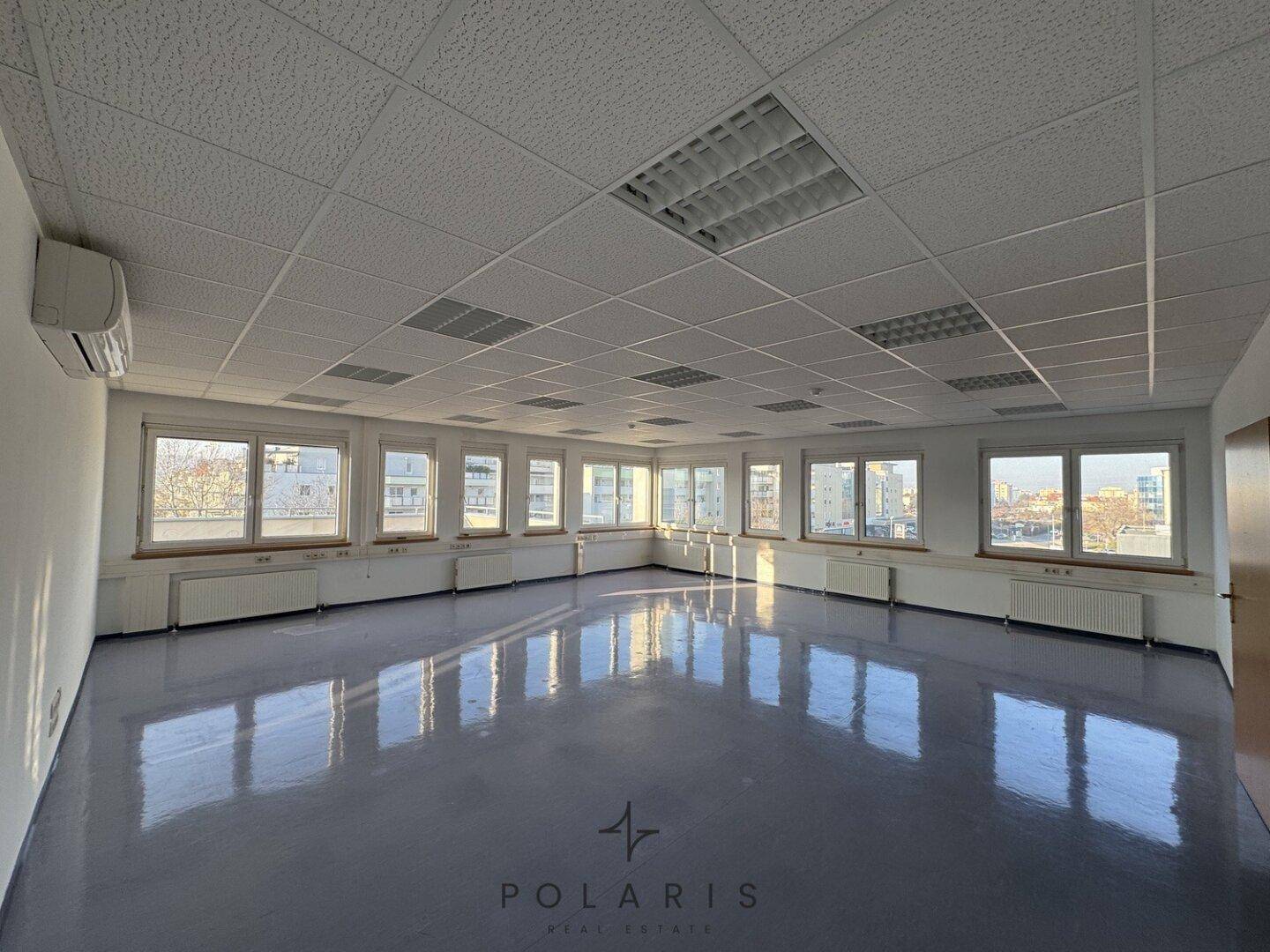 Helles und weitläufiges Büro mit zahlreichen Fenstern und einem reflektierenden Bodenbelag.