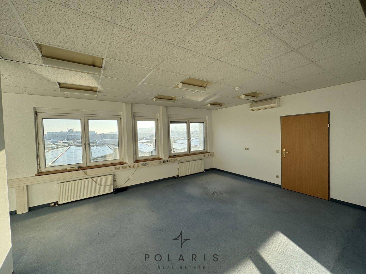 Büro mit Teppichboden, mehreren Fenstern und einer Holztür.