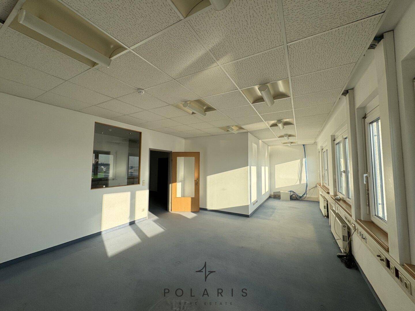 Langes Büro mit Teppichboden, Fenstern und einer Trennwand mit Glas.
