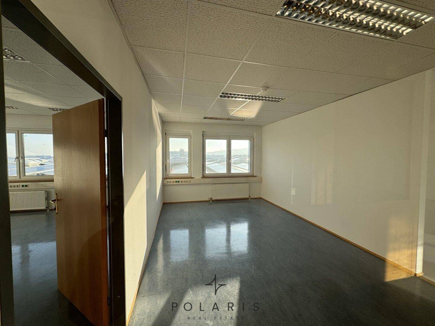 Funktionales Büro mit einer Holztür, großen Fenstern und einem pflegeleichten Vinylboden.