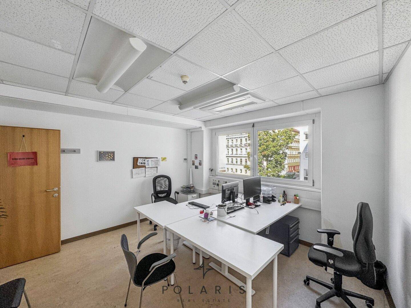 Helles Einzelbüro mit zwei Arbeitsplätzen, Schreibtischen und Bürostühlen, mit Blick nach draußen.