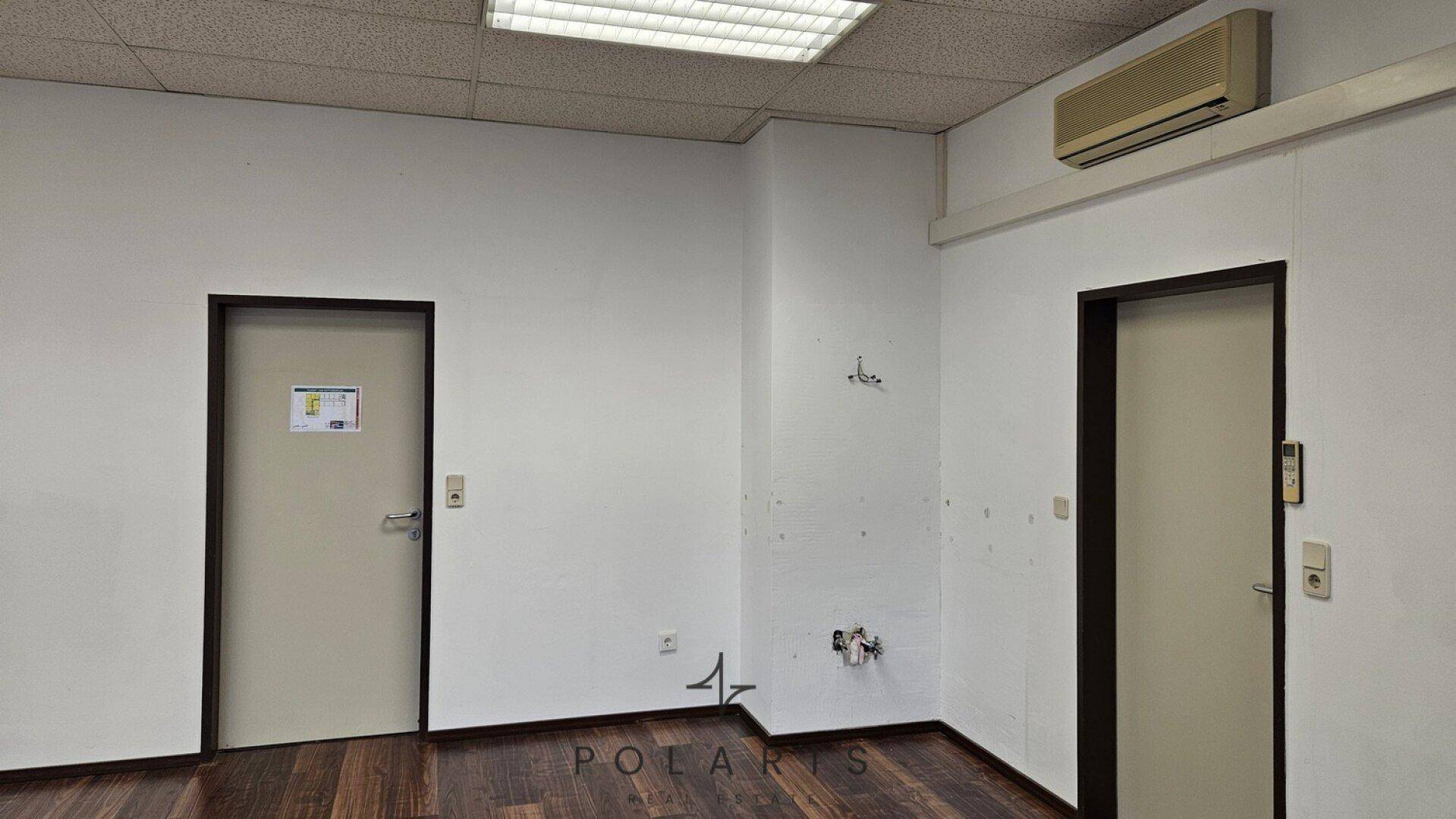 Büroansicht mit zwei Türen, einer Klimaanlage an der Wand und sichtbaren Anschlüssen, bereit für die Einrichtung.