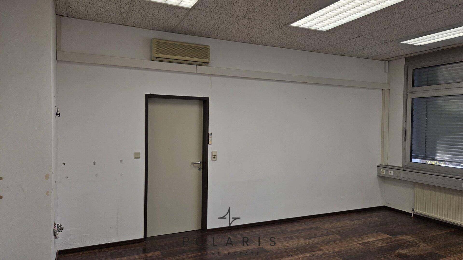 Weitere Perspektive des Büros mit einer Tür, Klimaanlage und einem Teil der Fensterfront, funktional und hell.