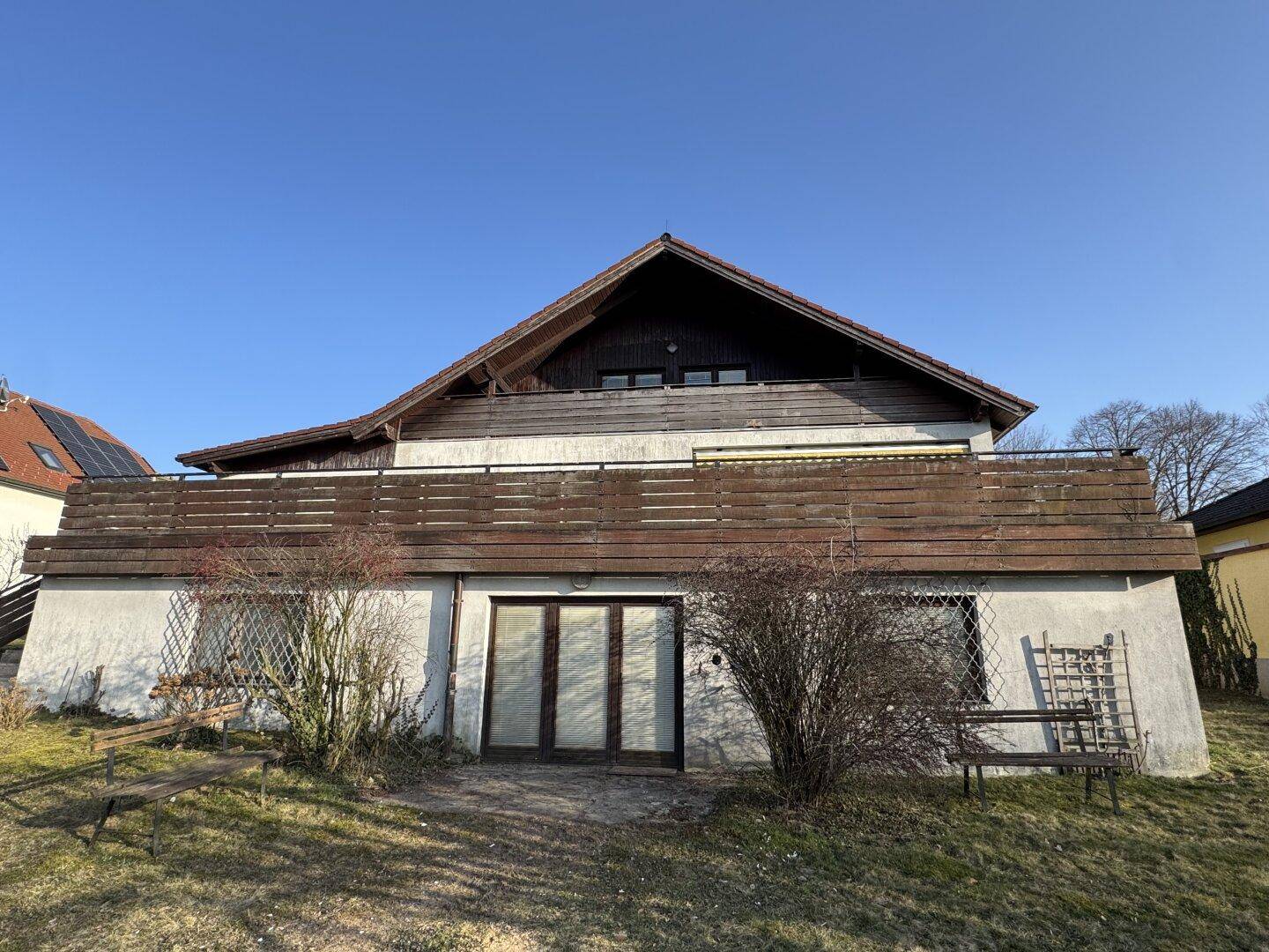 Vorderansicht des Hauses mit großer Terrasse im Obergeschoss und Zugang zum Gartenbereich.