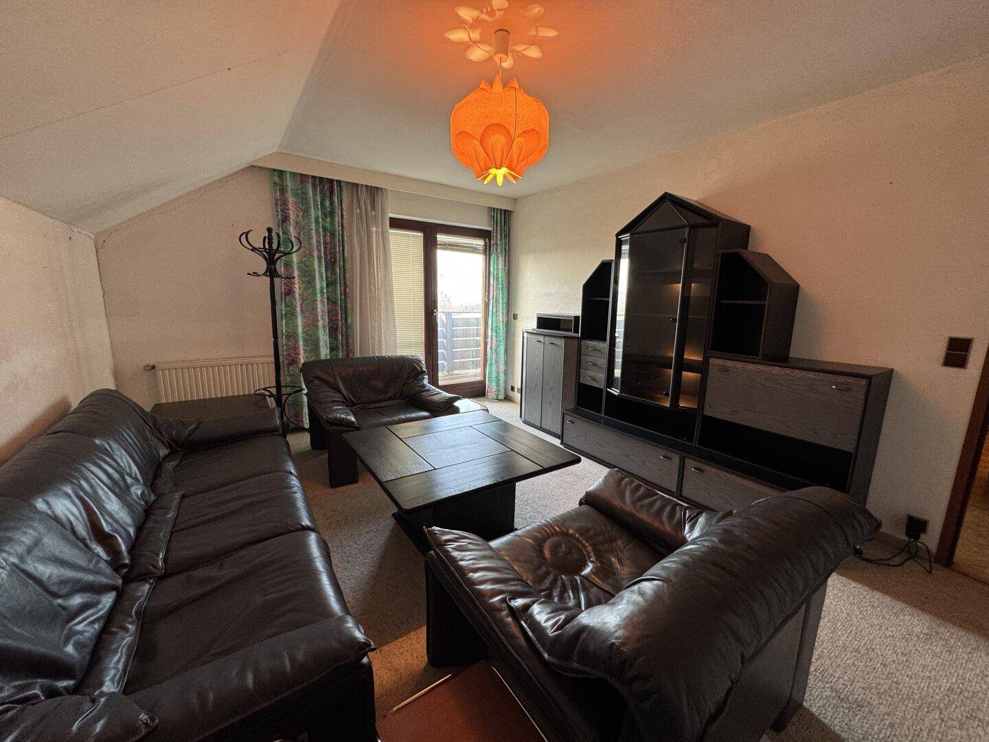 Gemütliches Wohnzimmer mit Ledersofas, Teppichboden und Zugang zu einem Balkon.