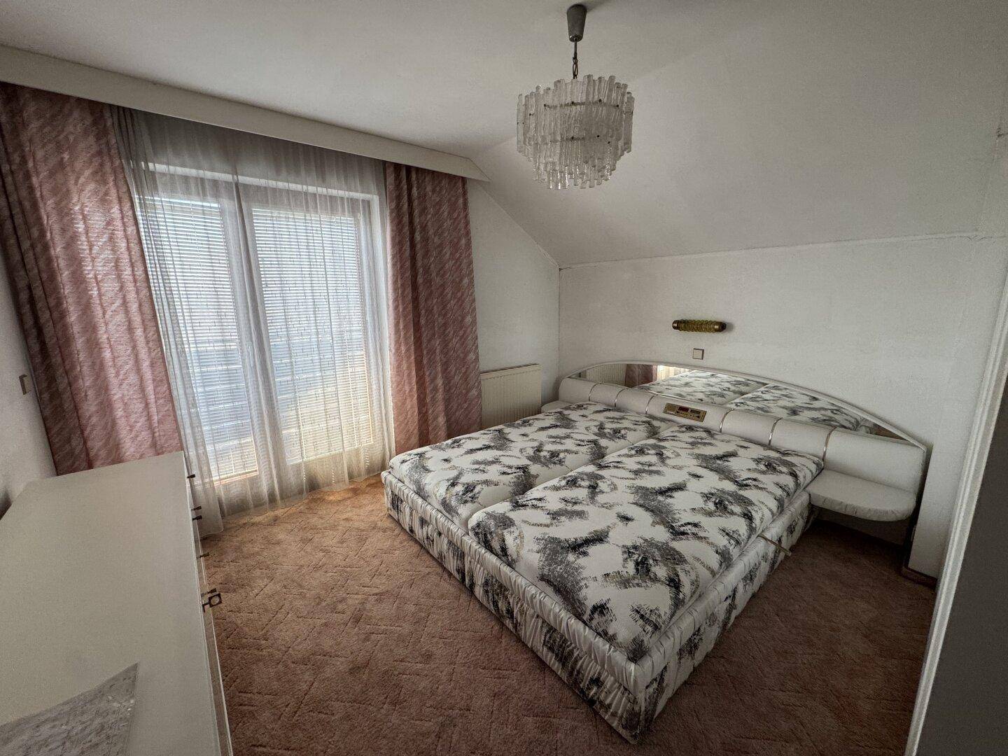 Schlafzimmer mit Doppelbett, Teppichboden und großem Fenster für viel Tageslicht.
