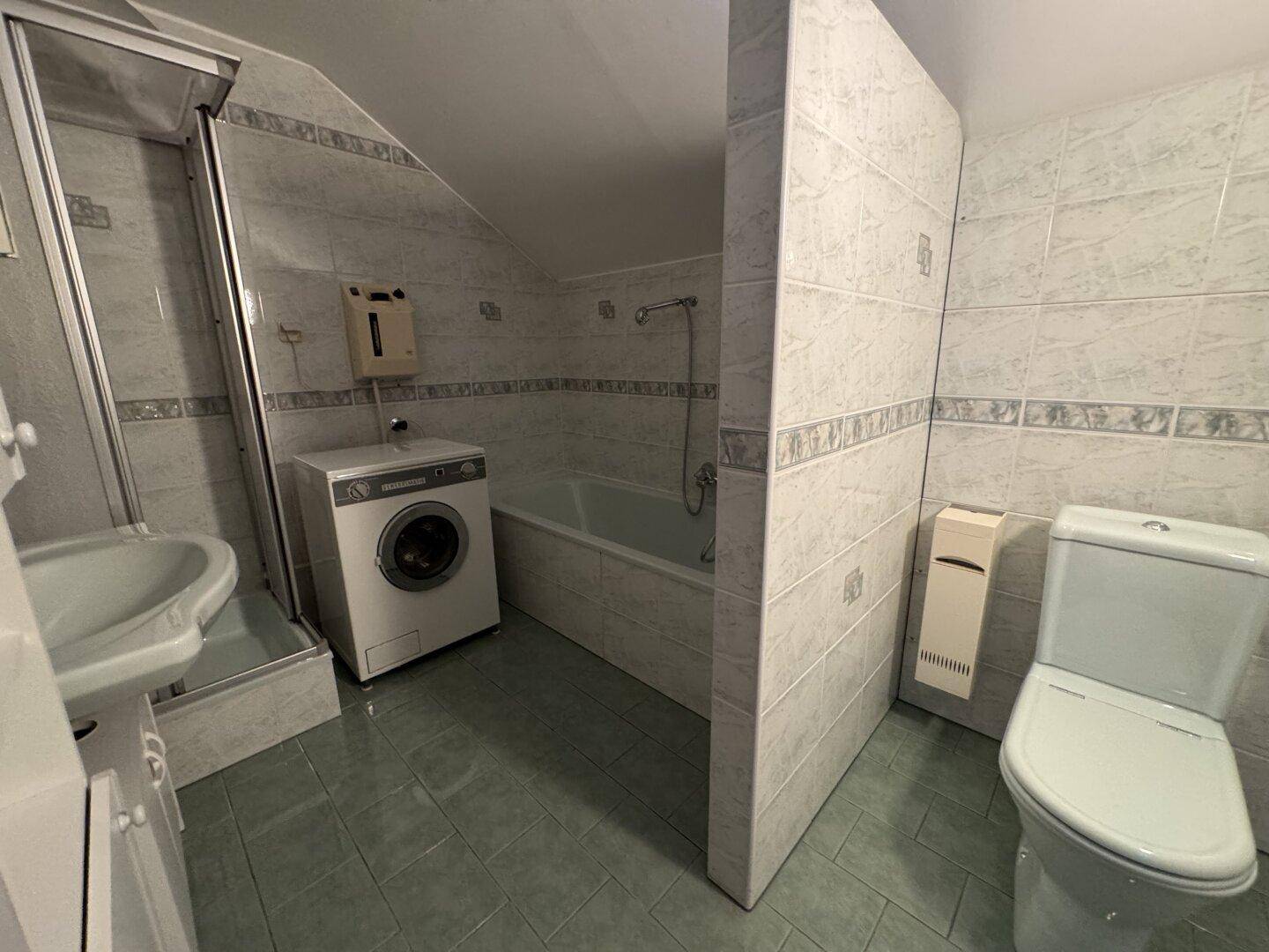 Badezimmer mit Dusche, Badewanne, WC und Waschmaschine unter Dachschräge.