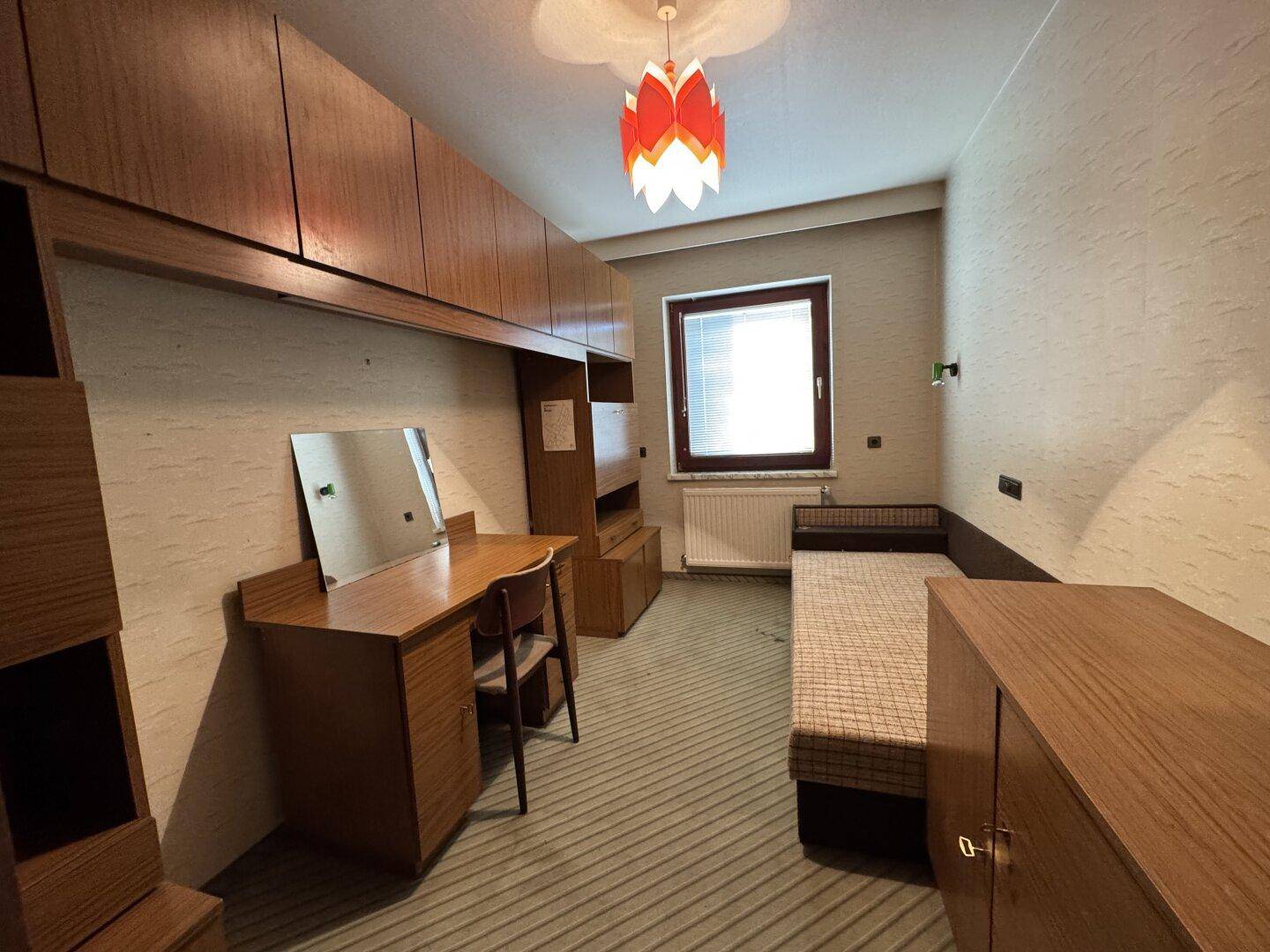 Kleines Schlafzimmer oder Arbeitszimmer mit Einzelbett, Schreibtisch und Einbauschränken.
