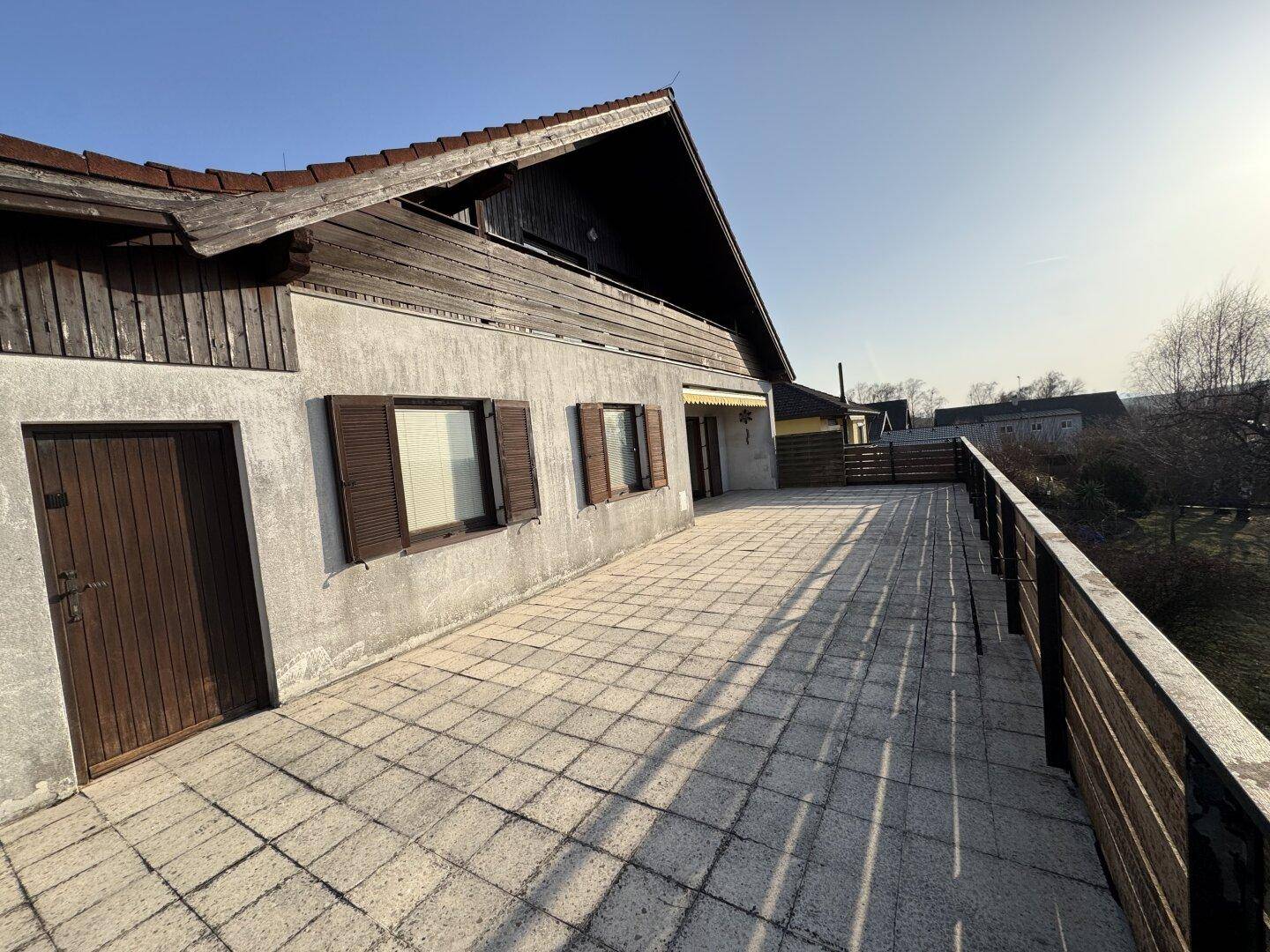 Große geflieste Terrasse mit Holzzaun und Blick auf die Umgebung, ideal für Outdoor-Aktivitäten.