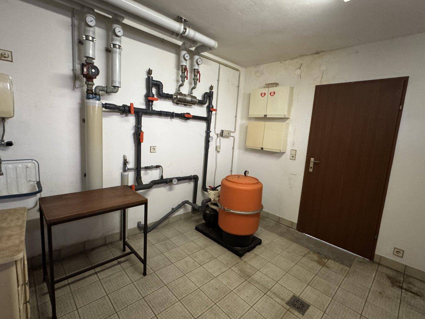 Technikraum im Keller mit Heizungsanlage, Rohren und Wasserinstallationen.