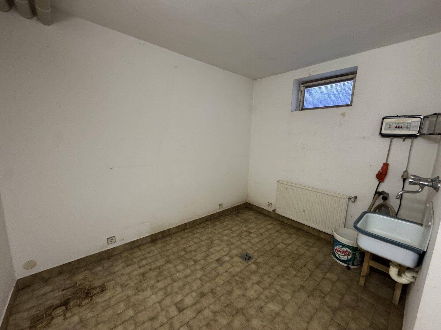 Einfacher Kellerraum mit Fenster, Waschbecken und Fliesenboden, ideal als Abstellraum.