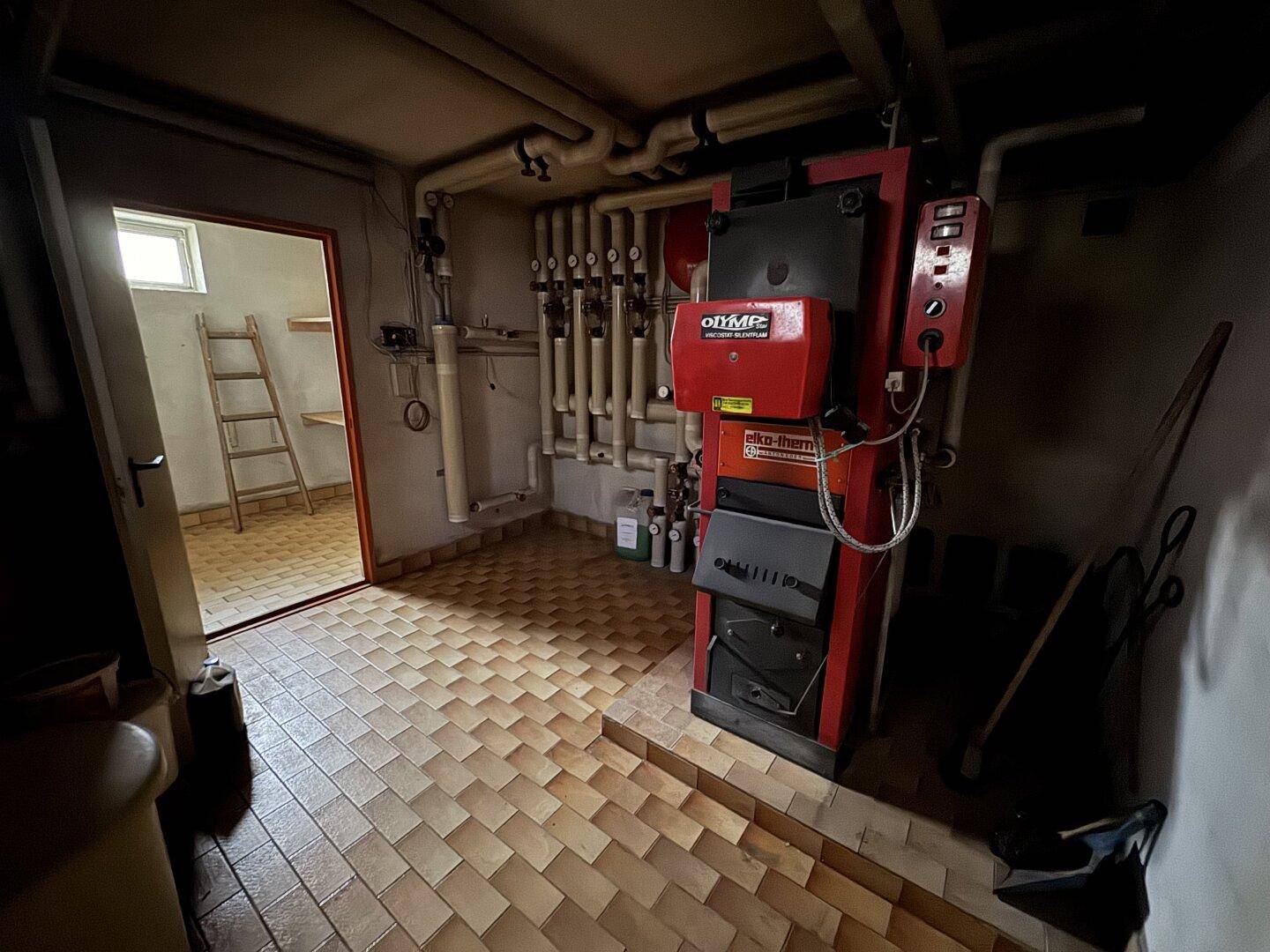 Heizungsraum im Keller mit großem Ölkessel und Zugang zu einem weiteren Raum.