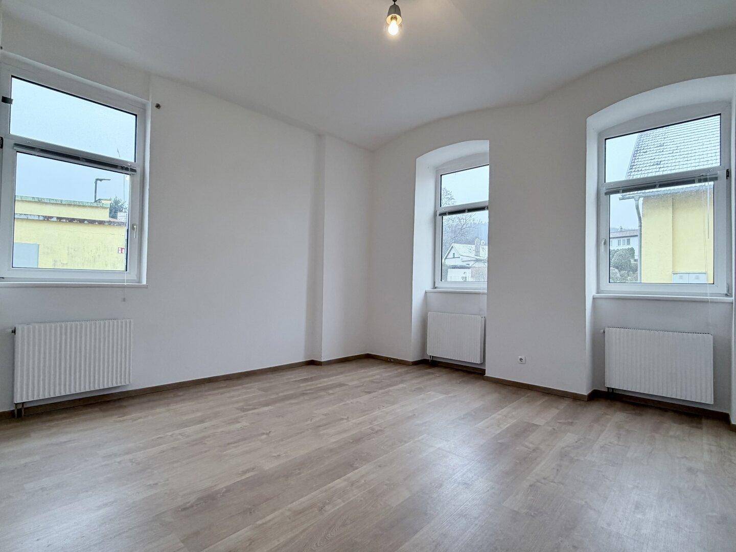 Lichtdurchfluteter Raum mit drei Fenstern und hellem Laminatboden, ideal für Wohnzwecke.