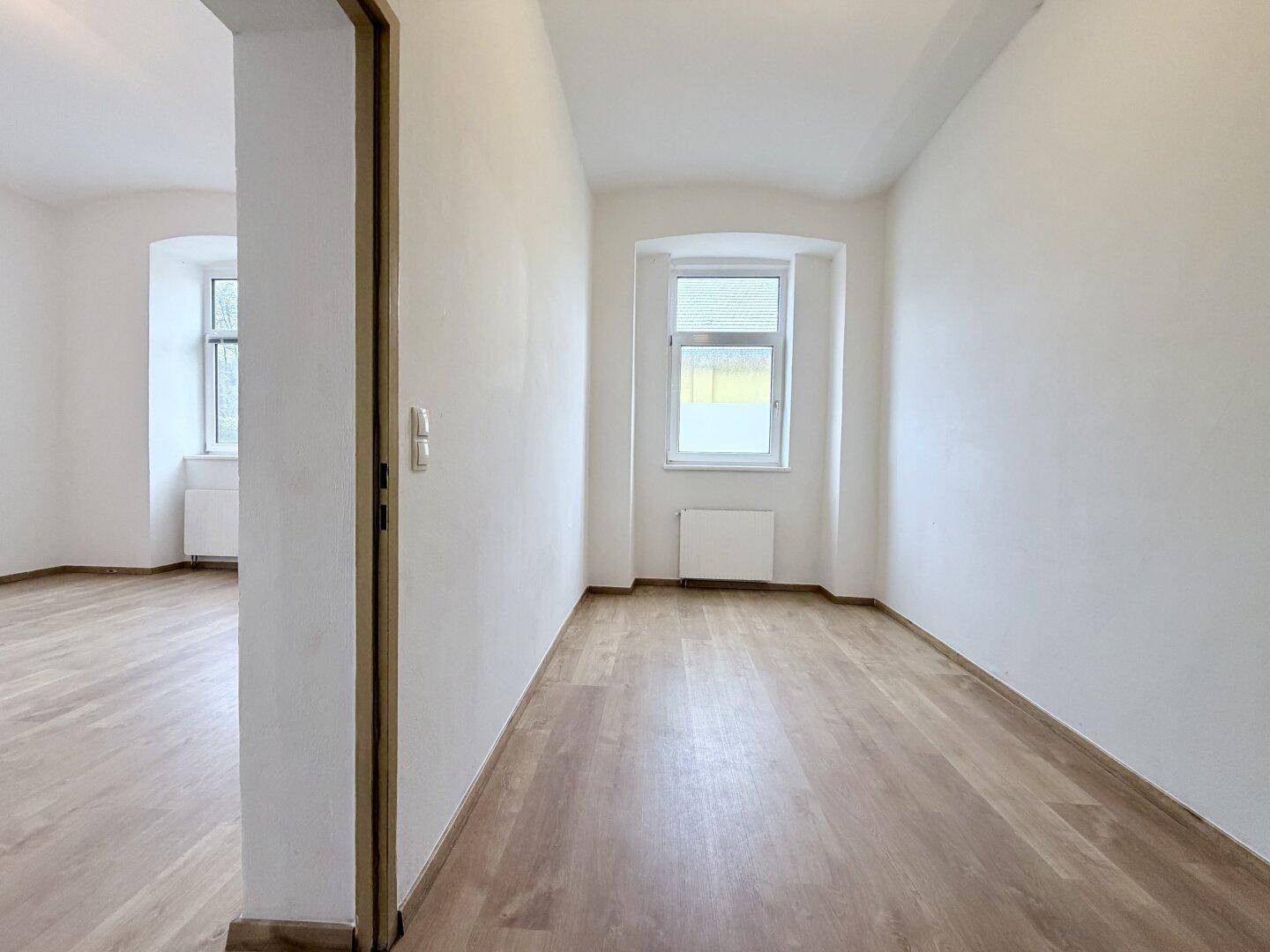 Langer Flur mit Laminatboden und einem Fenster, der zu weiteren Räumen führt.