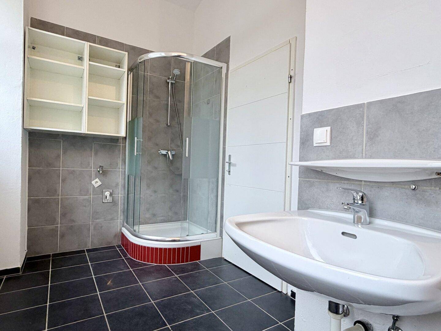 Modernes Badezimmer mit Duschkabine, Waschbecken und grauen Wandfliesen, in gutem Zustand.