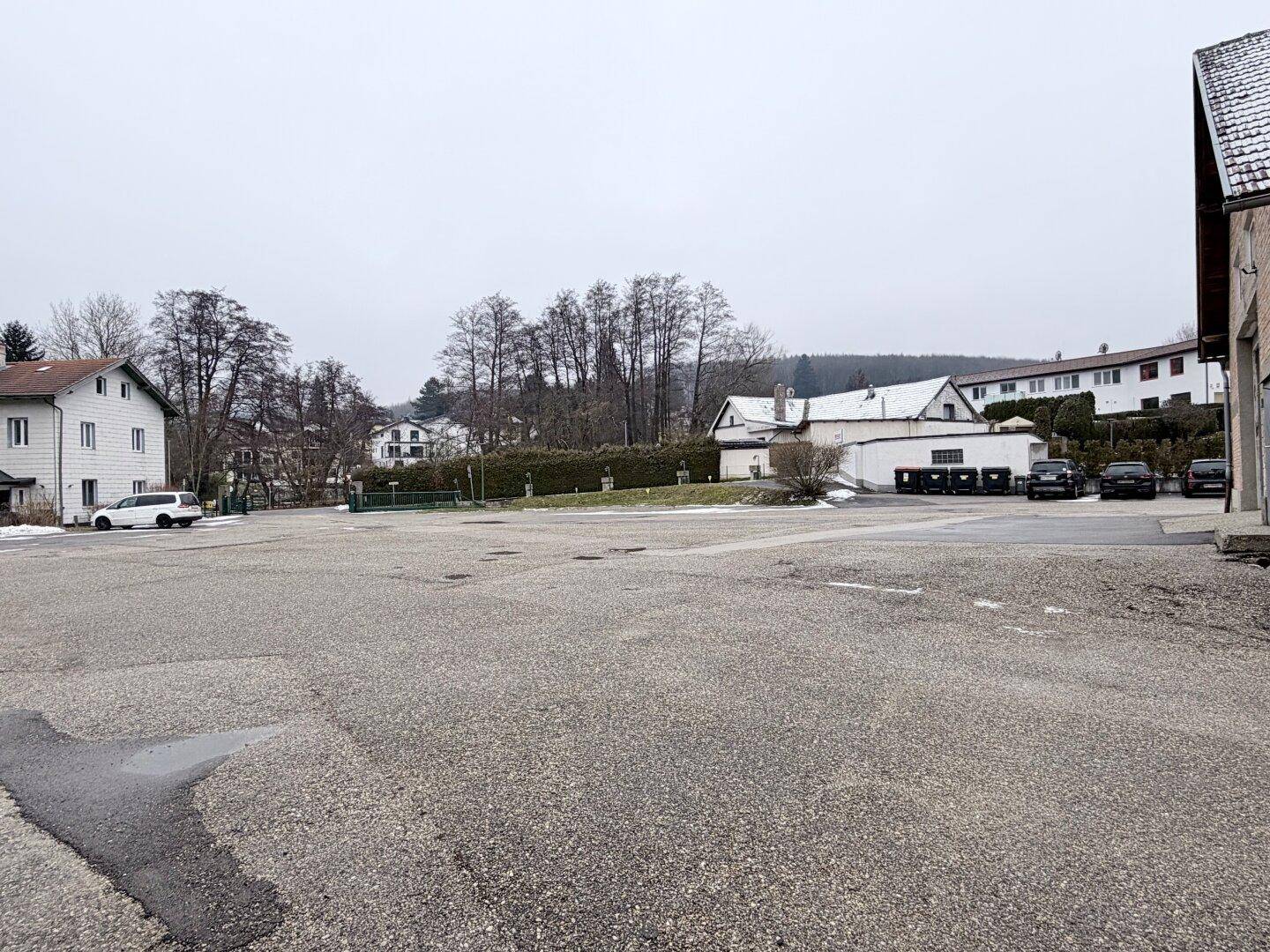 Großer Schotterparkplatz vor dem Gebäude mit umliegenden Häusern und Bäumen im Winter.