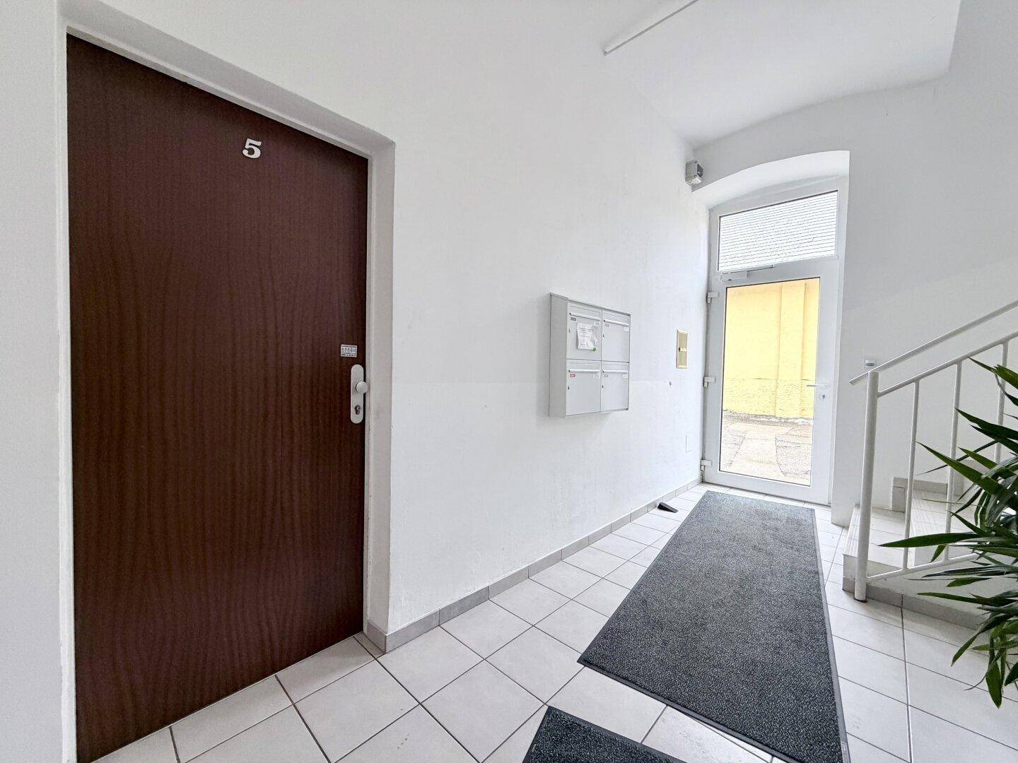 Eingangsbereich mit Fliesenboden, Briefkästen und Treppenaufgang, führt zur Wohnungstür Nummer 5.