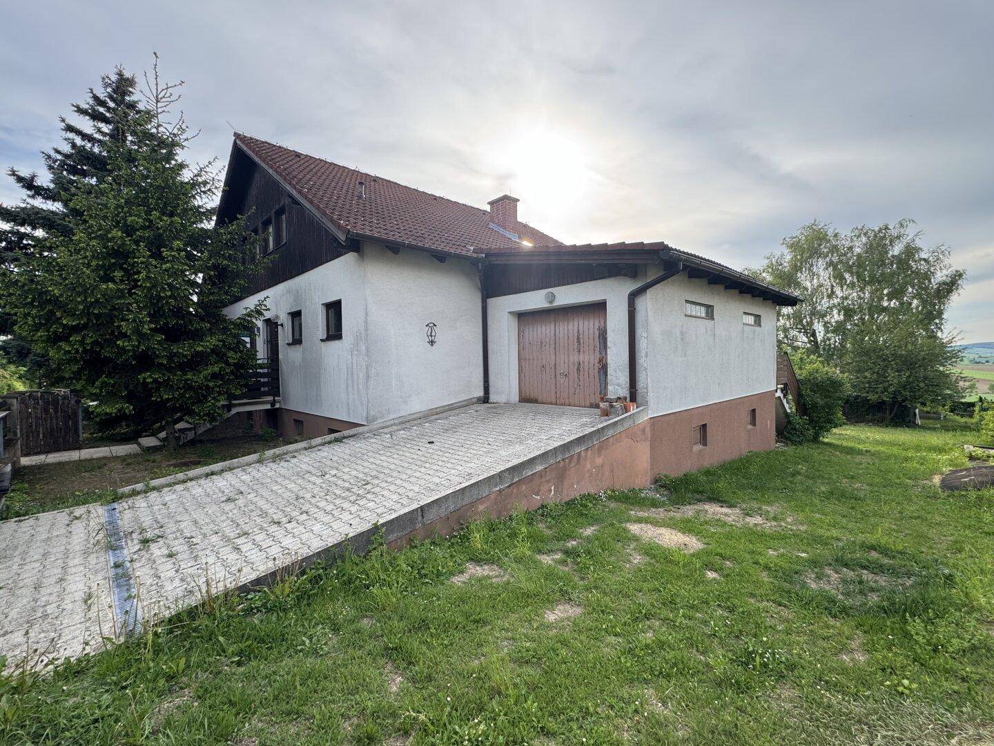 Seitenansicht des Hauses mit Garage, Auffahrt und umgebender Grünfläche.