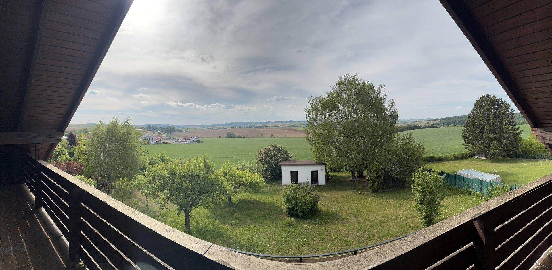 Panoramablick von einem Balkon über weite Felder und die ländliche Umgebung unter bewölktem Himmel.