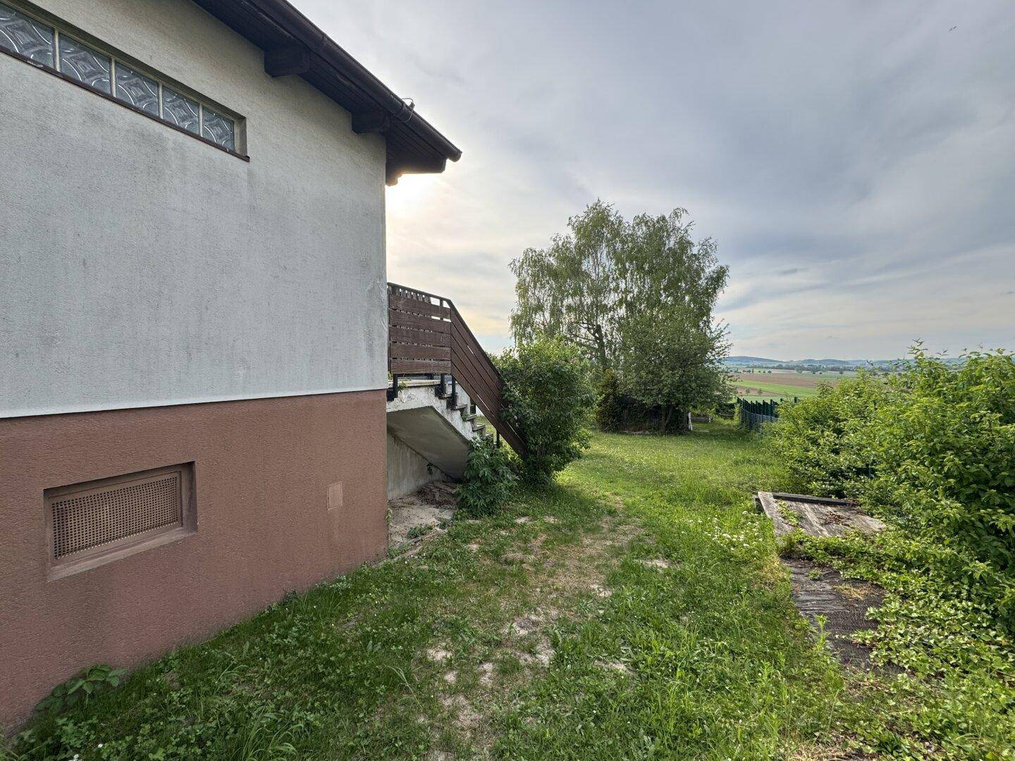 Seitenansicht des Hauses mit Außentreppe und weitläufigem Gartenbereich.