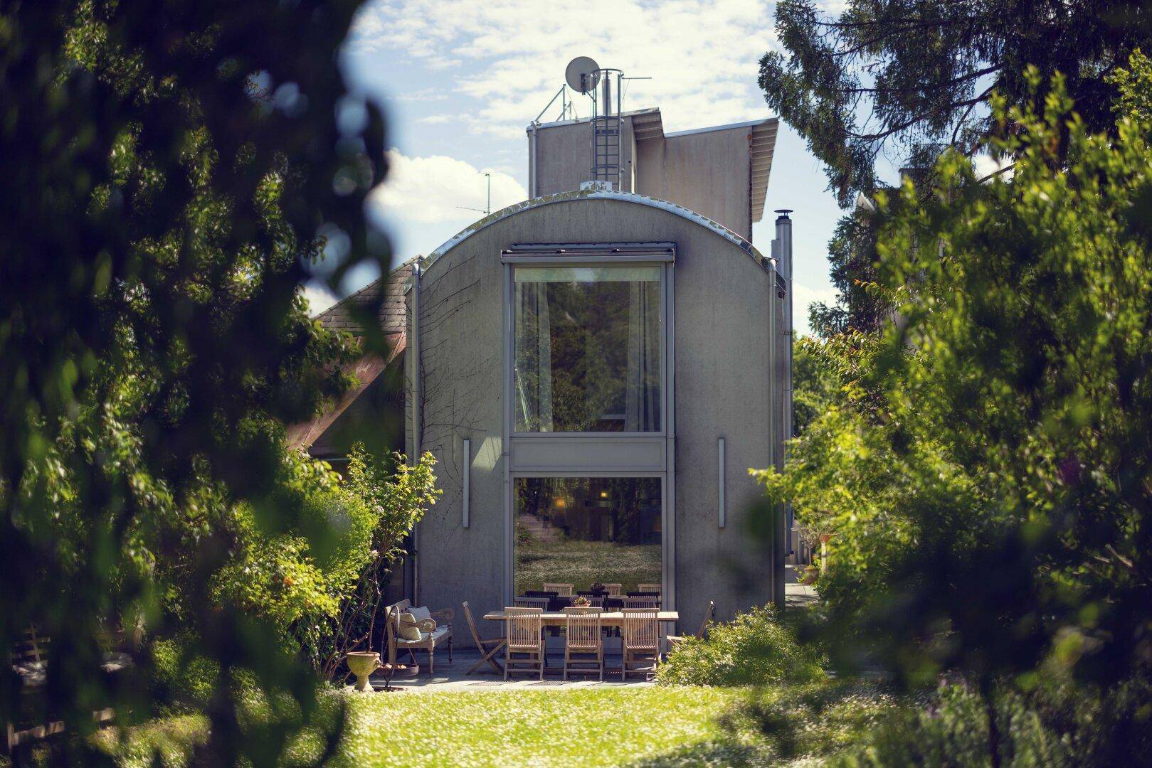 Ansicht des modernen Hauses vom Garten aus, mit großen Fenstern und einer möblierten Terrasse.