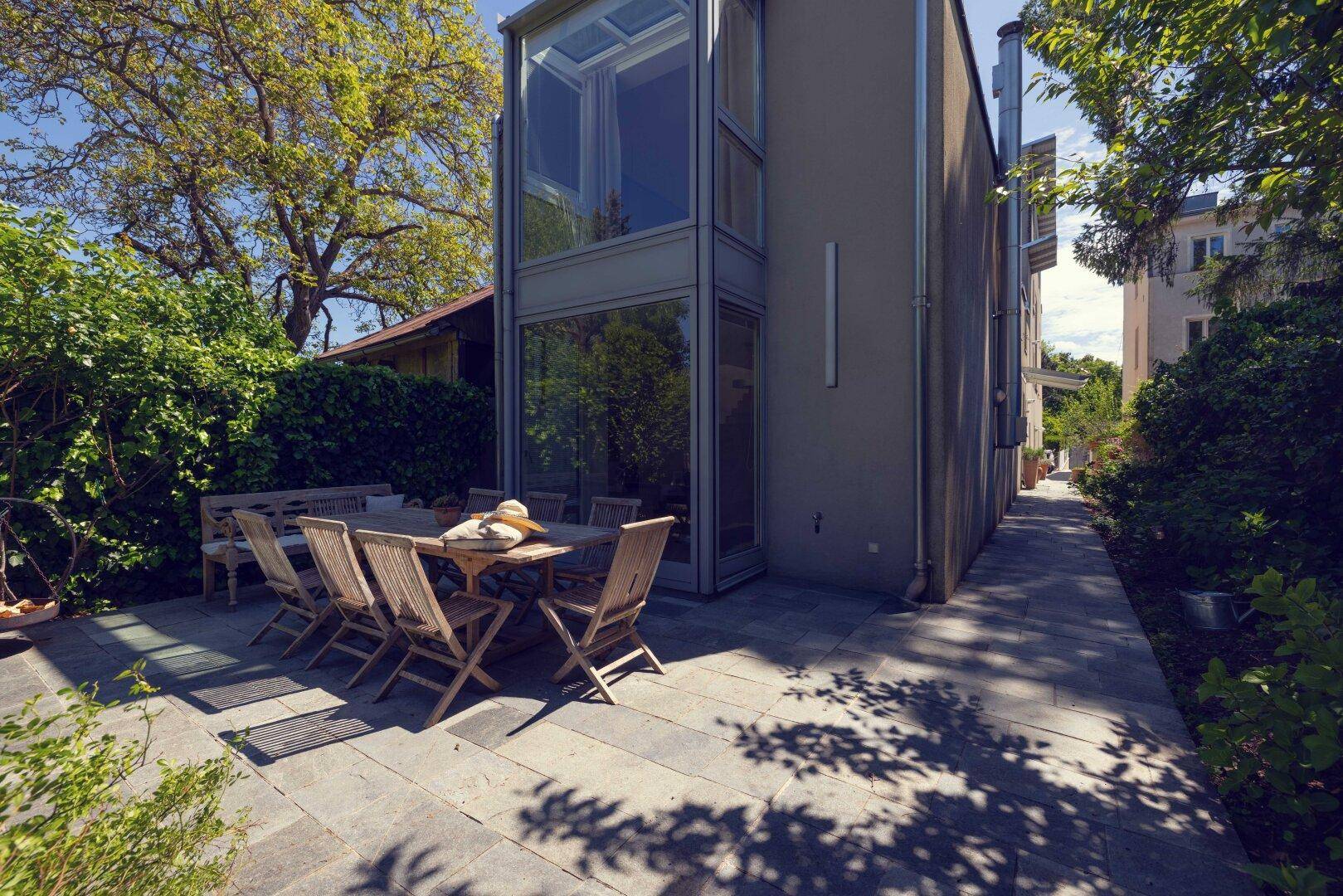 Seitenansicht des modernen Hauses mit möblierter Terrasse und gepflastertem Weg entlang der Glasfassade.