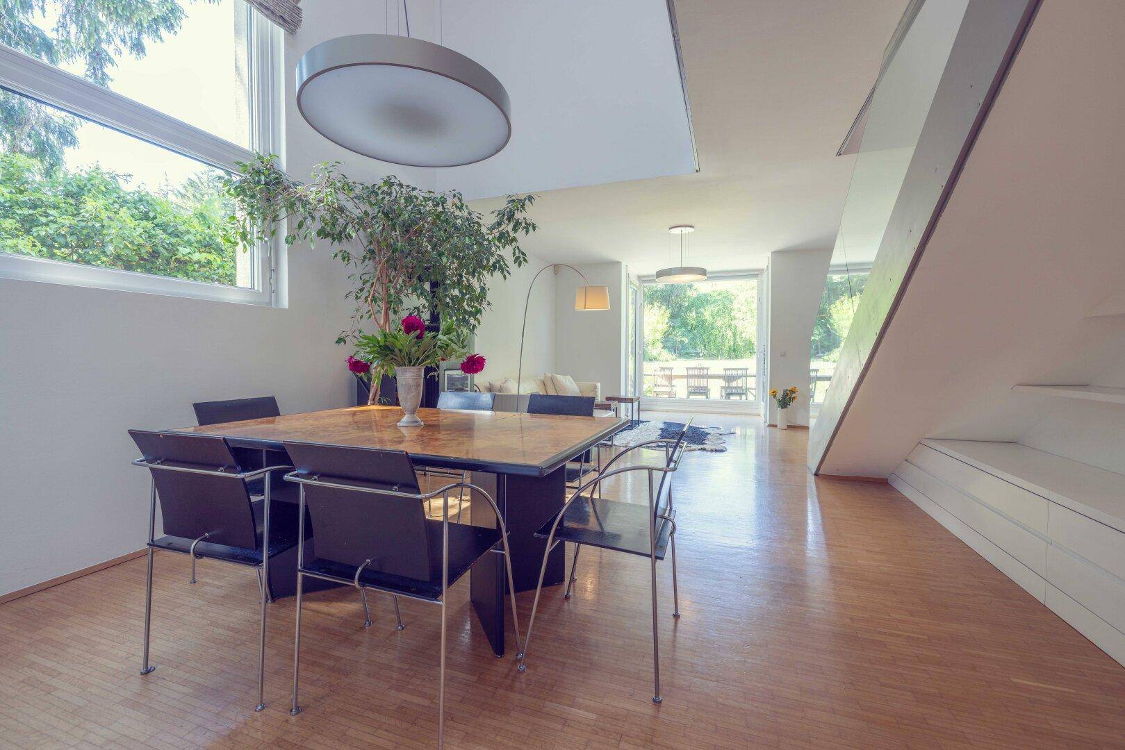 Moderner Essbereich mit großem Holztisch und schwarzen Stühlen, direkt am Fenster mit Gartenblick.