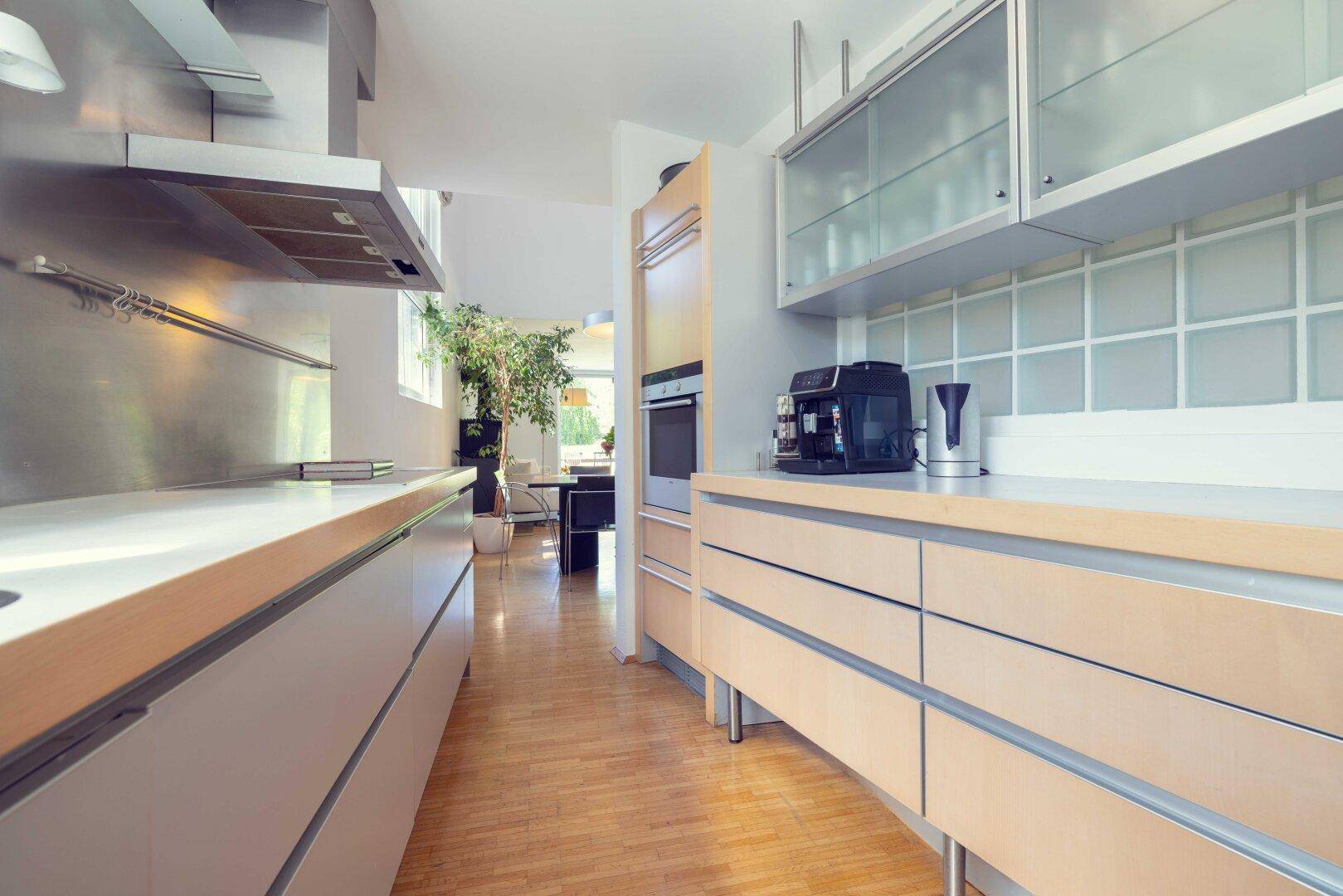 Moderne Küche mit hellen Holzfronten, Edelstahlgeräten und Blick in den offenen Wohnbereich.