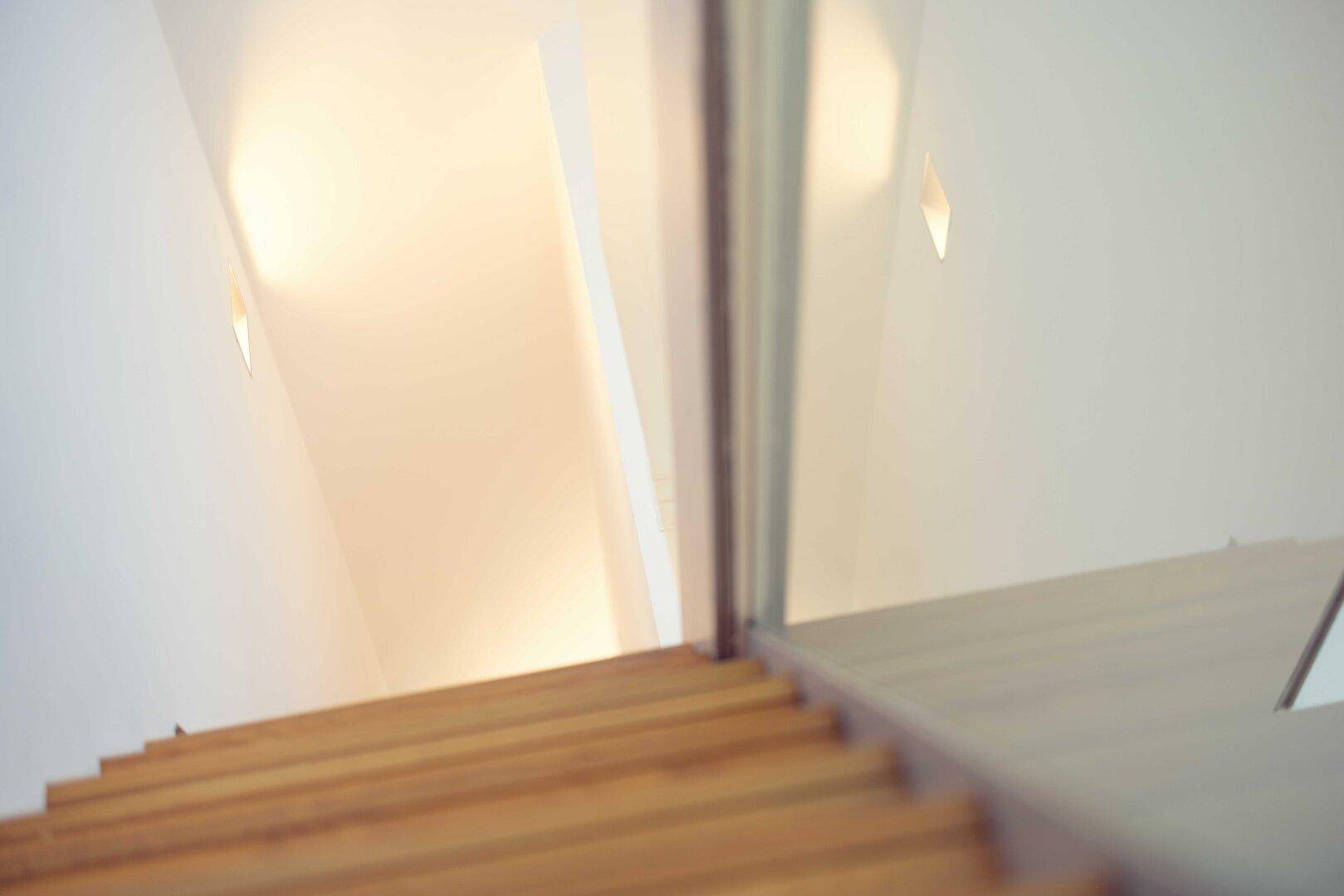 Moderne Holztreppe mit Glasgeländer und indirekter Beleuchtung im Treppenhaus.