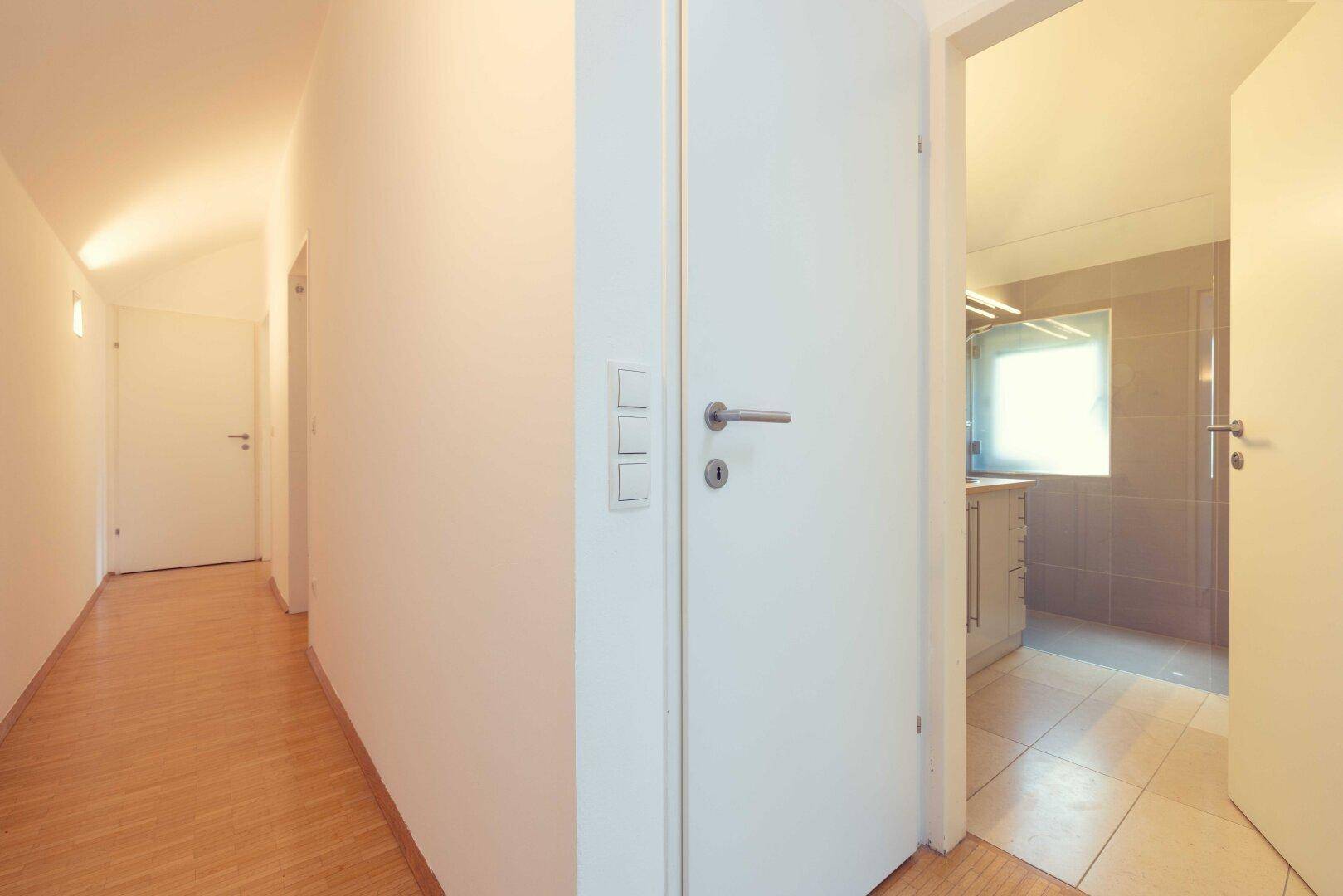 Heller Flur mit Holzboden und Zugang zu verschiedenen Zimmern, inklusive Badezimmer.