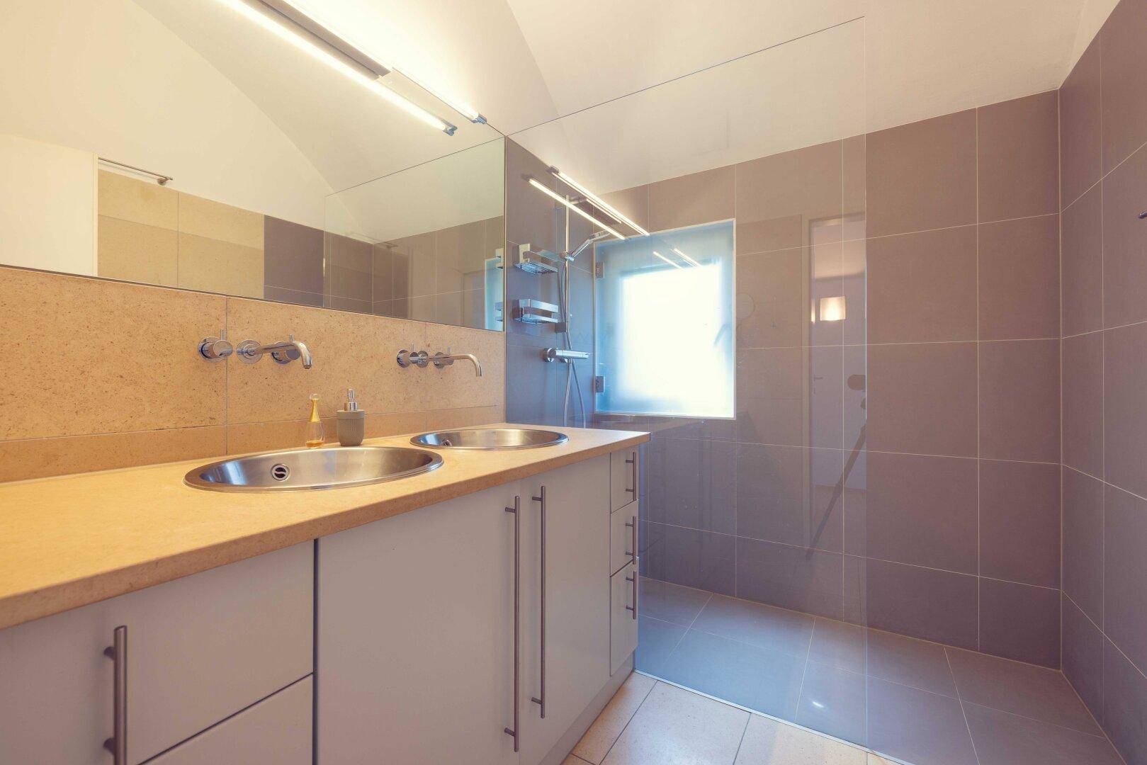 Modernes Badezimmer mit Doppelwaschbecken, großer Spiegelfläche und Duschbereich mit Fenster.
