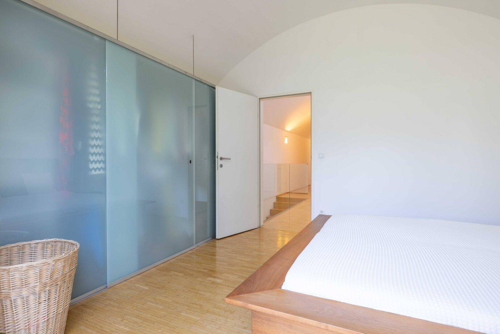 Schlafzimmer mit Holzbett, Schiebetürenschrank aus Milchglas und Zugang zum Flur.
