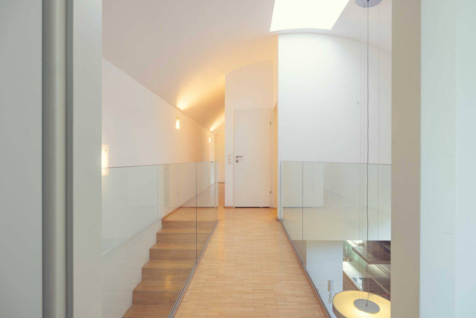 Heller Flur im Obergeschoss mit Glasgeländer, Gewölbedecke und viel Tageslicht.