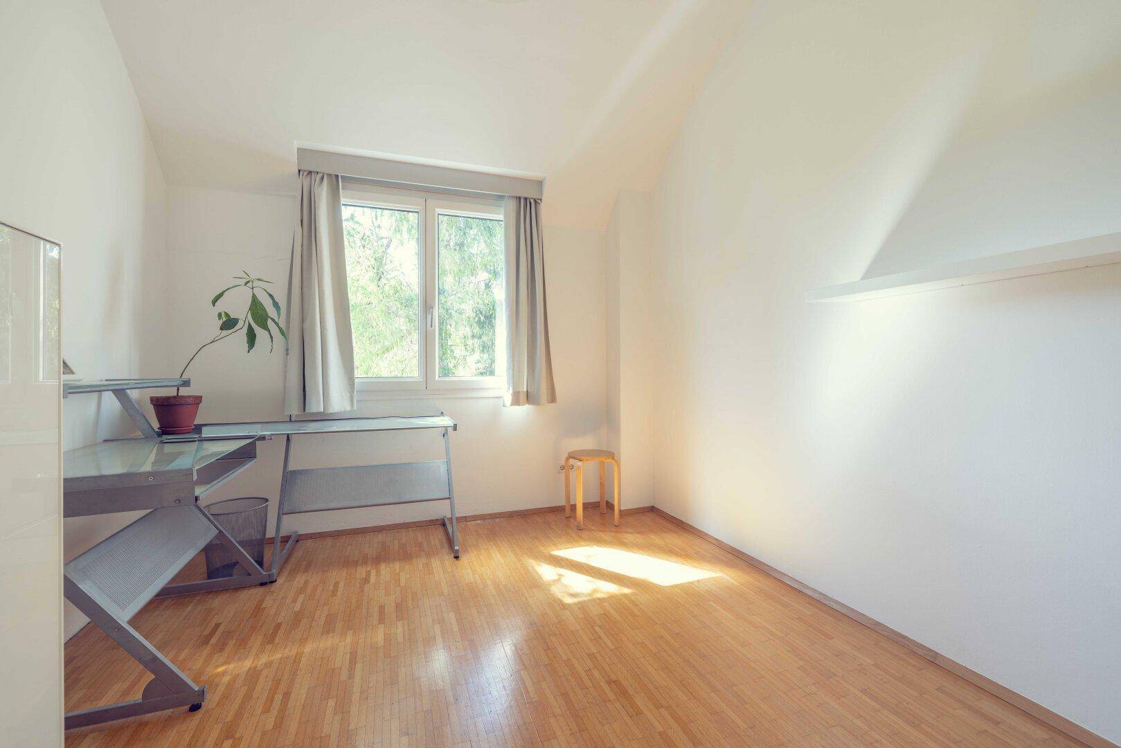 Helles Zimmer mit Holzboden, Fensterblick ins Grüne und modernem Schreibtisch.