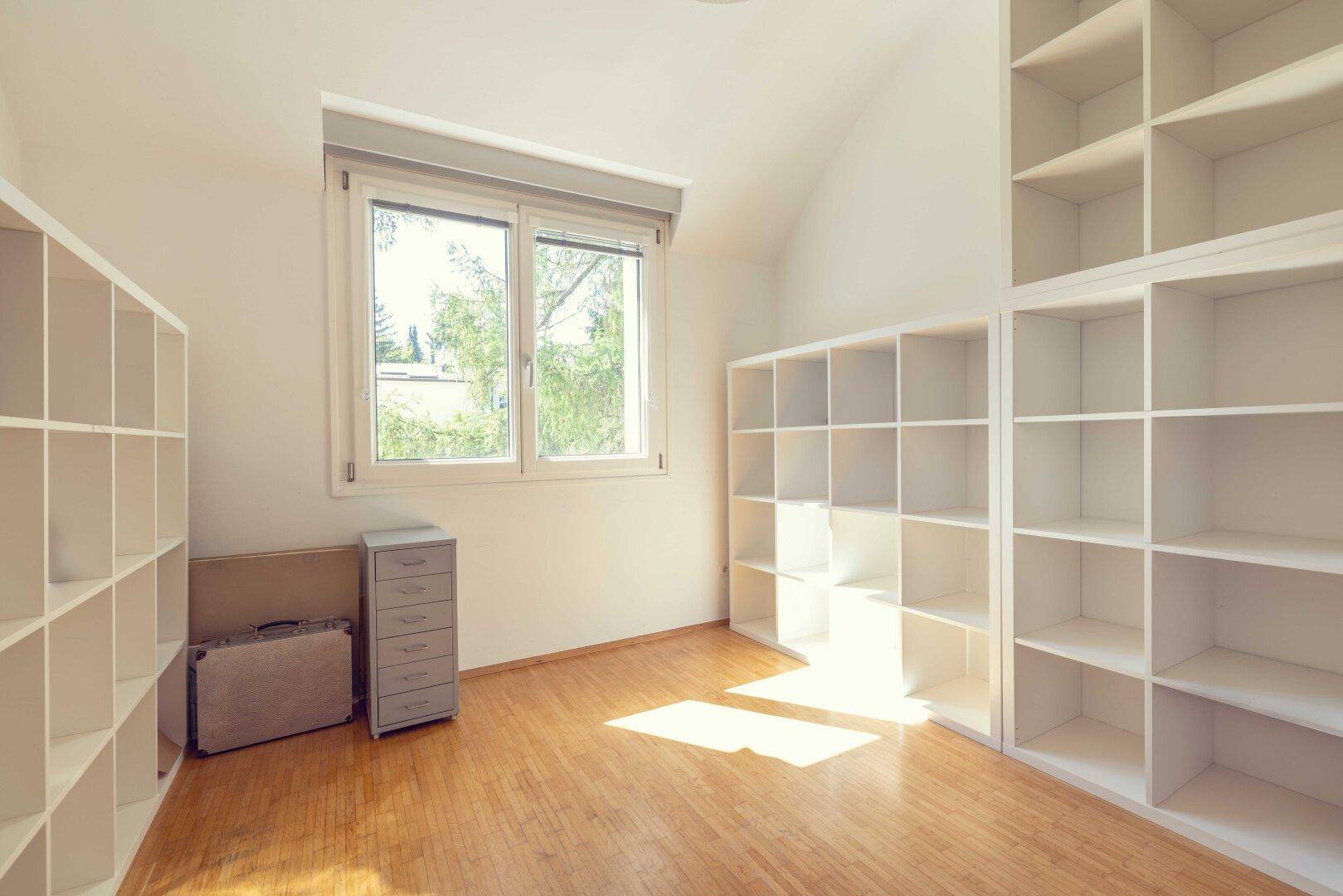 Geräumiges Zimmer mit Holzboden, Fenster und weißen modularen Regalsystemen.