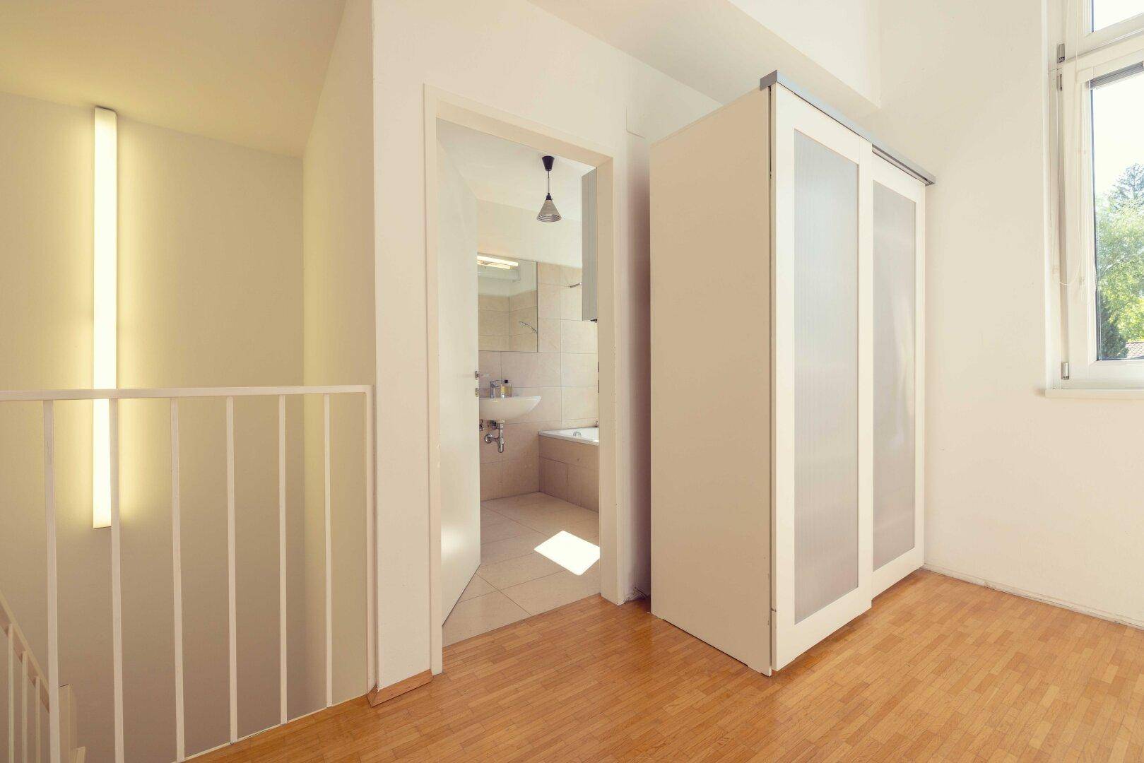 Heller Flur mit Holzboden und Zugang zu einem Badezimmer mit Badewanne.