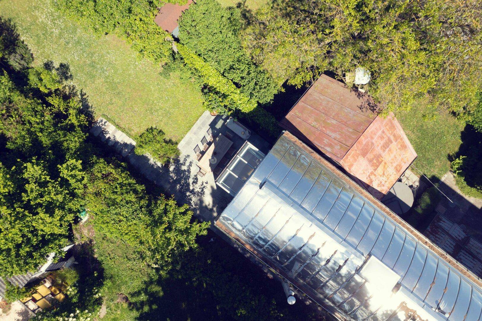 Luftaufnahme eines Anwesens mit großem Gewächshaus, Rasenflächen und altem Baumbestand.