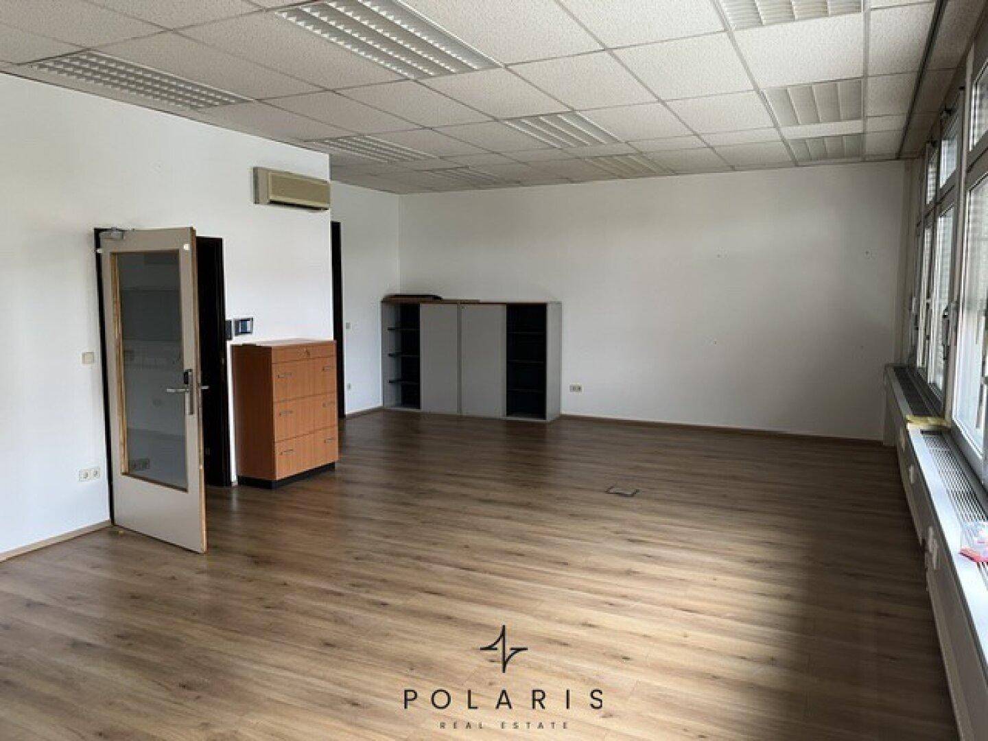 Helles Büro mit großen Fenstern, Laminatboden und abgehängter Decke, ideal für Arbeitsbereiche.