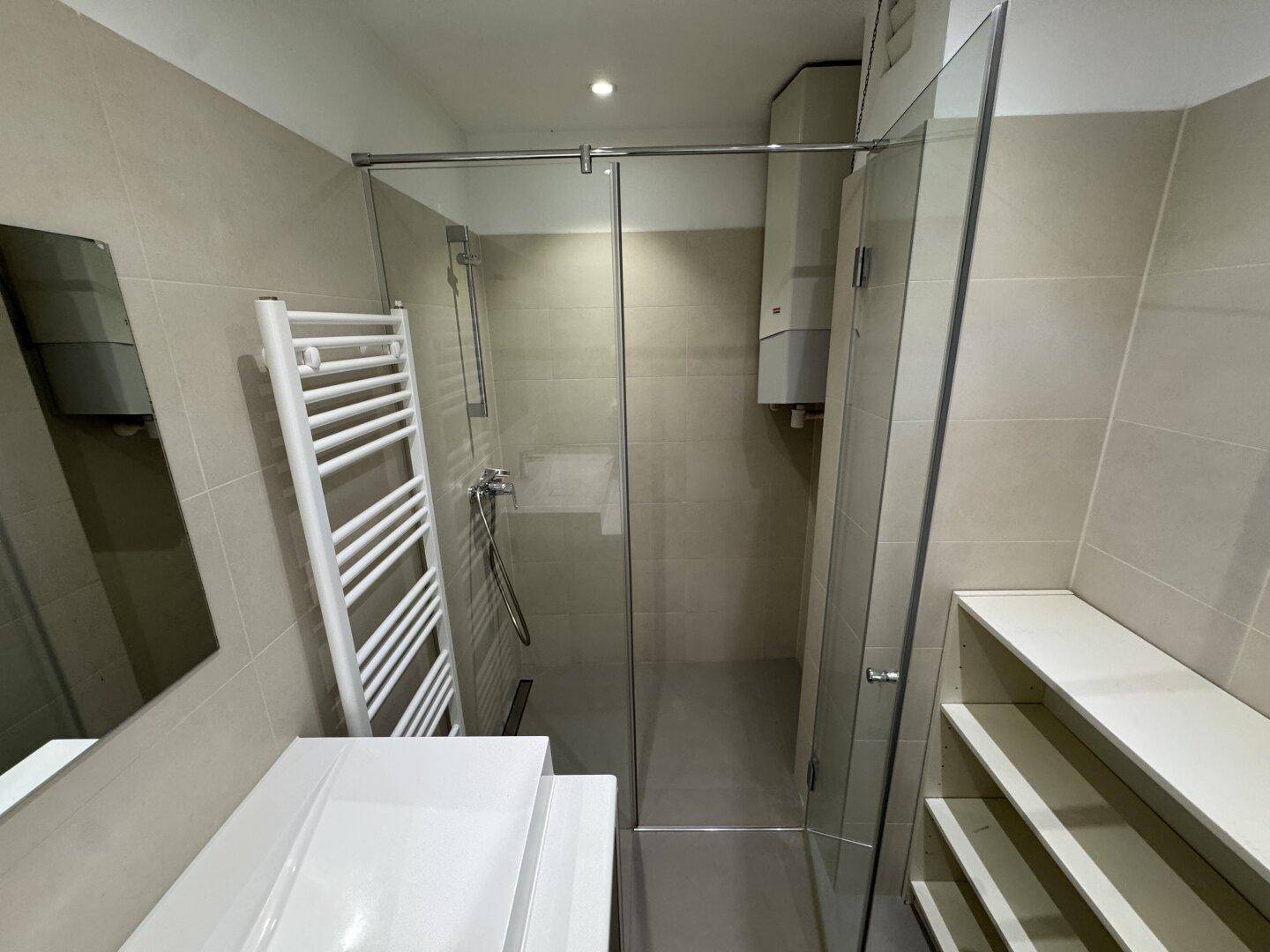 Duschbereich im modernen Badezimmer mit Glasabtrennung, beheiztem Handtuchhalter und hellen Wandfliesen.