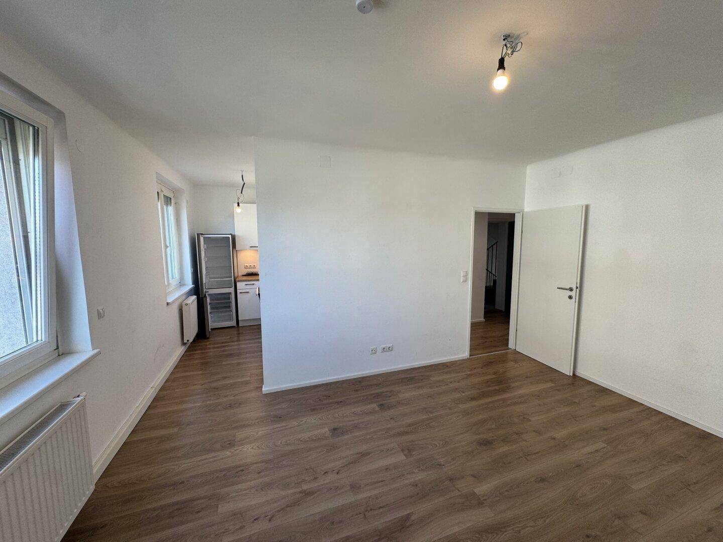Heller Wohnbereich mit Laminatboden und offenem Übergang zur modernen Küche.