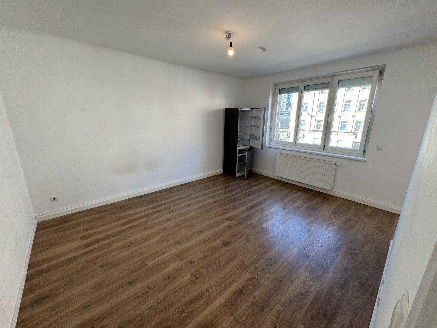 Geräumiger, heller Wohnbereich mit Laminatboden und großem Fenster, offen zur Küche.