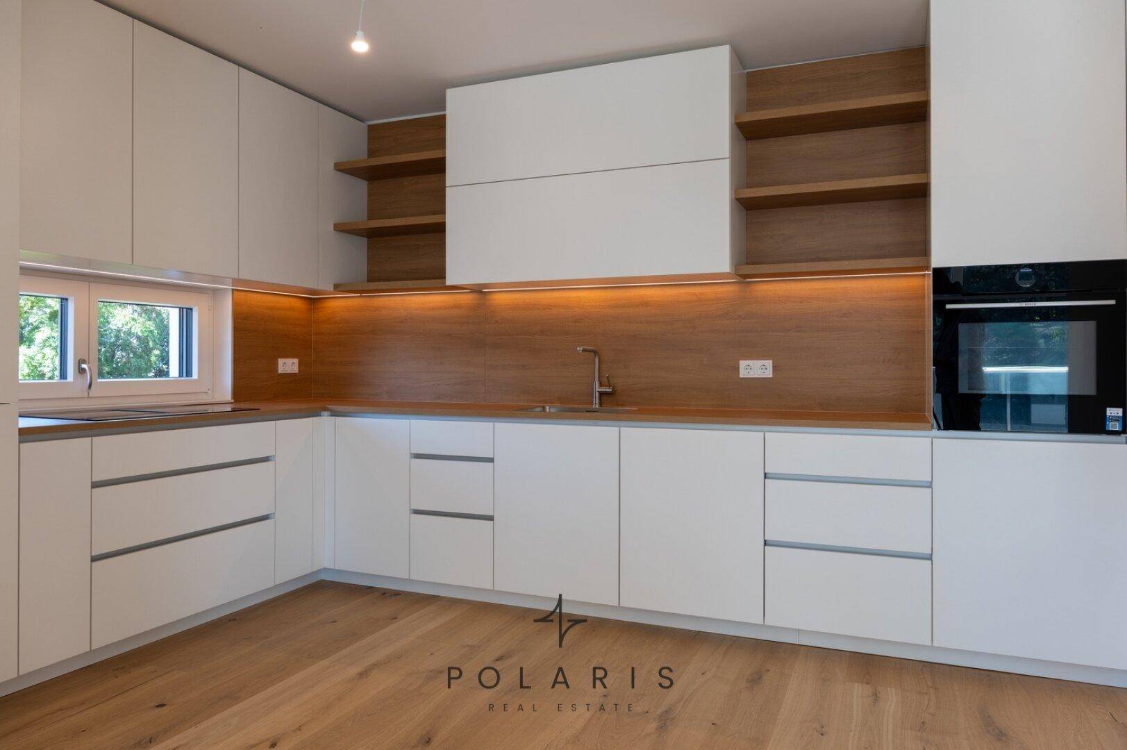 Helle, moderne Küche mit weißen Fronten, Holzdetails und integriertem Backofen, bereit zur Nutzung.