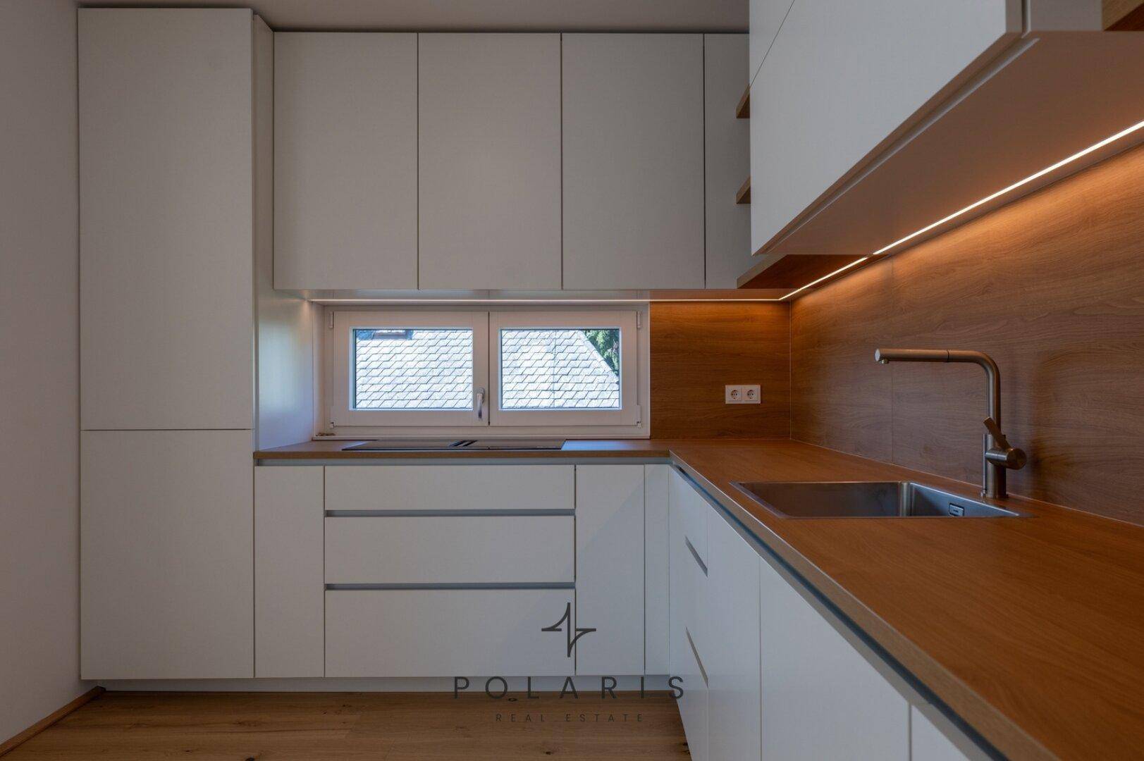 Detailansicht der modernen Küche mit Holz-Arbeitsplatte, Spüle und Fenster, das Tageslicht hereinlässt.