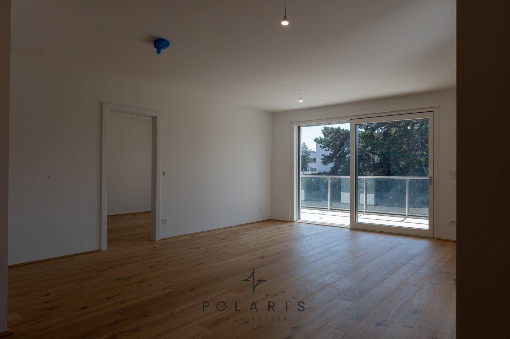 Helles Wohnzimmer mit Holzboden und großen Schiebetüren zum Balkon, bietet einen weiten Blick.